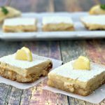 2 keto lemon bars on parchment paper with 3 lemons bars on a white plate