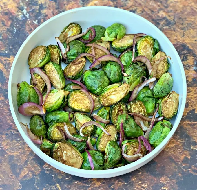 roasted air fryer balsamic brussels sprouts in an air fryer with sliced red onions