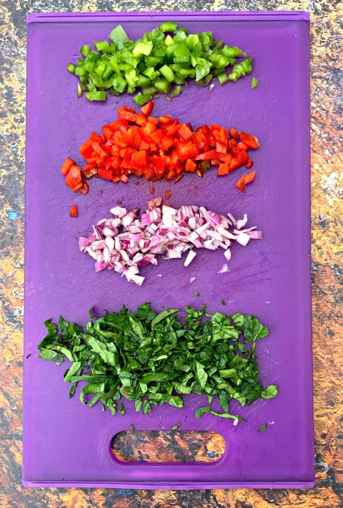 chopped spinach, peppers, and onion on a purple cutting board
