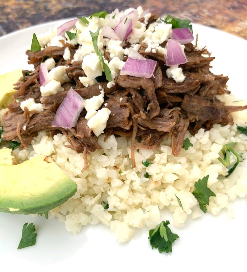 keto low carb instant pot barbacoa on top of cilantro lime cauliflower rice on a white plate