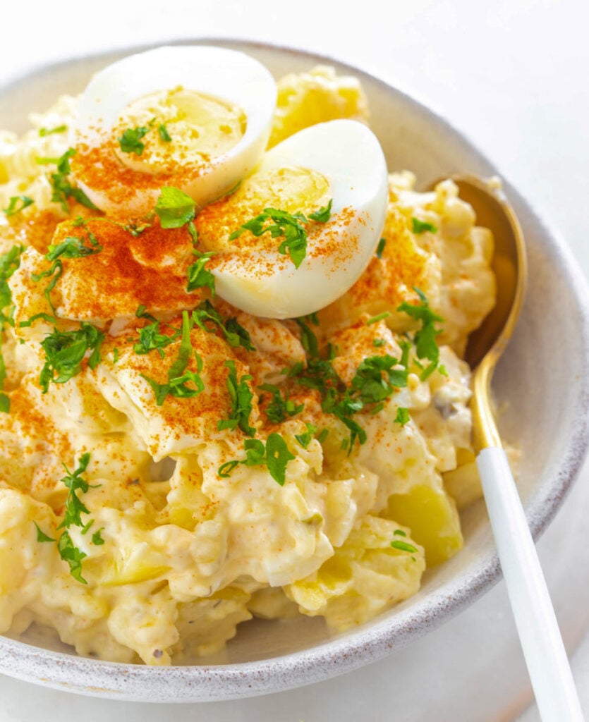 Instant Pot potato salad in a white bowl with boiled eggs and sprinkled with paprika