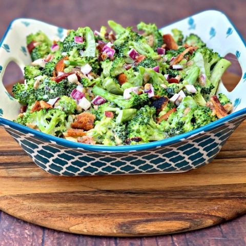 chopped broccoli with mayo, red onions, sunflower seeds, bacon, and sweetener in a blue bowl