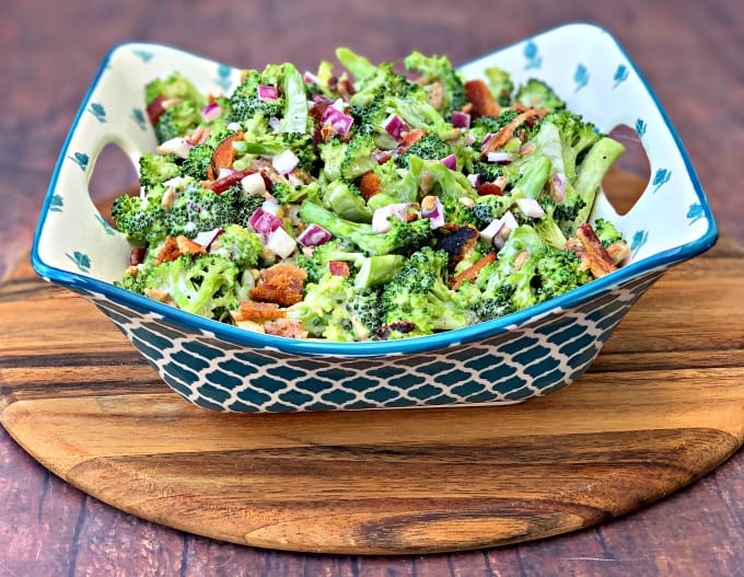 chopped broccoli with mayo, red onions, sunflower seeds, bacon, and sweetener in a blue bowl