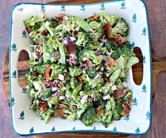 chopped broccoli with mayo, red onions, sunflower seeds, bacon, and sweetener in a blue bowl