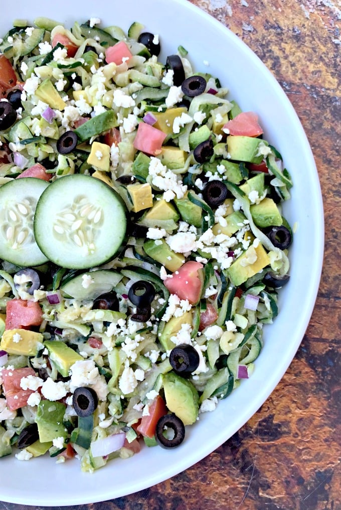 keto zucchini noodles pasta salad in a white bowl with tomatoes, olives, cucumbers, feta cheese, and red onions