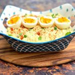 keto low carb potato salad with boiled eggs in a blue bowl on a wooden pizza paddle board