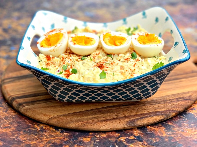 keto low carb potato salad with boiled eggs in a blue bowl on a wooden pizza paddle board