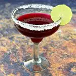 beet margarita in a glass with a sliced lime