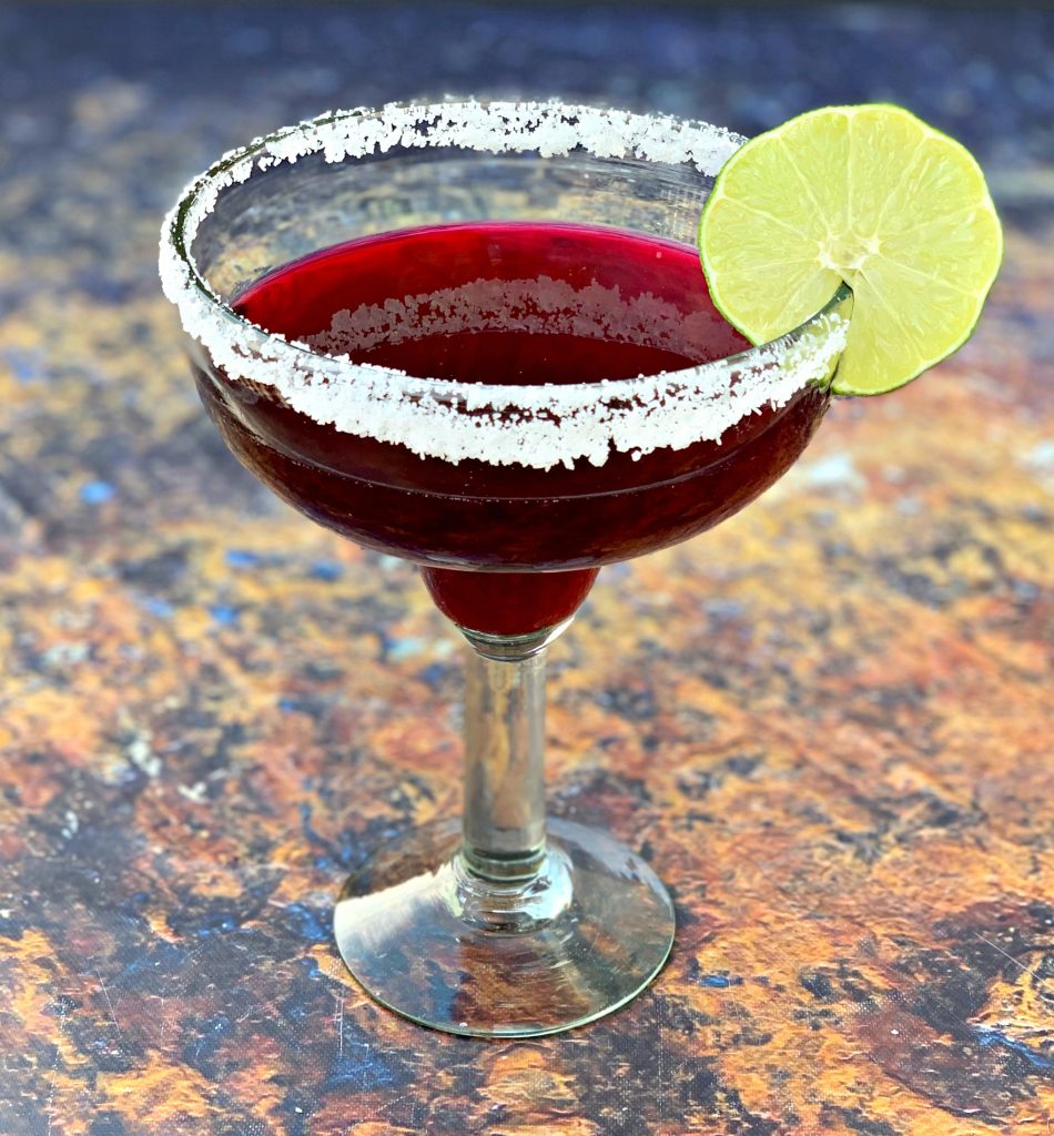 beet margarita in a glass with a sliced lime 