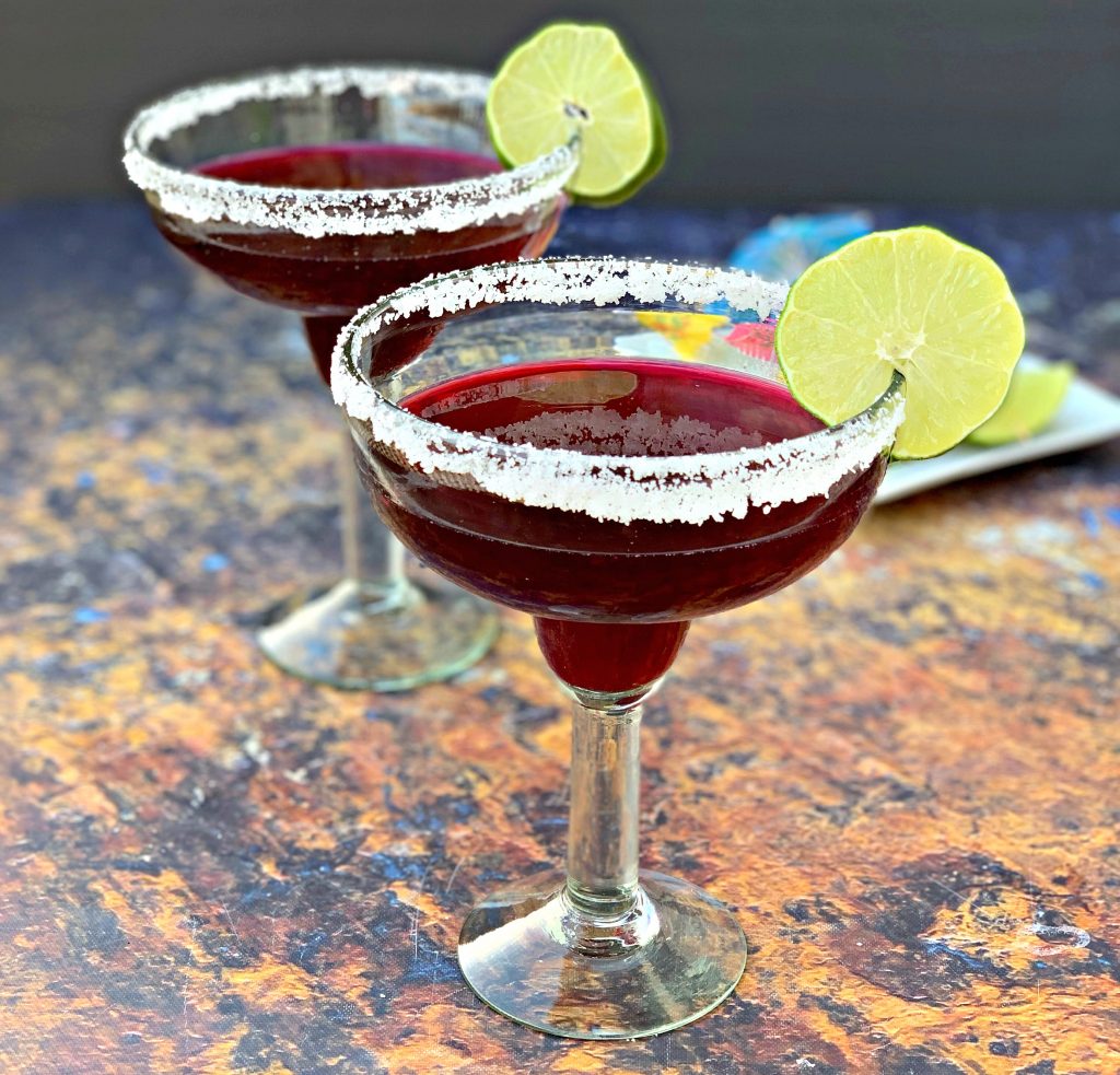 2 beet margaritas in a glass with sliced lime