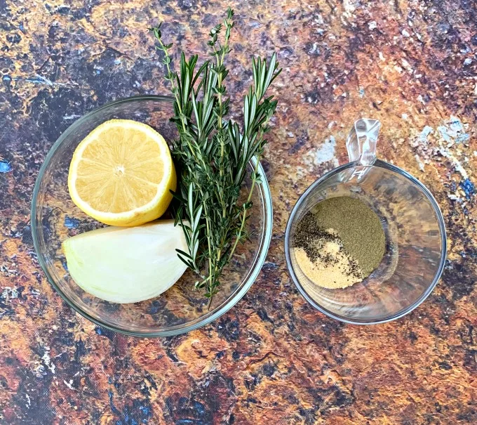 fresh lemon, onion, rosemary, and thyme in a glass bowl with seasonings for whole chicken