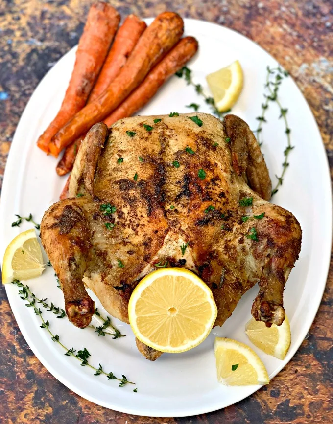 air fryer whole chicken on a white plate with fresh lemon and roasted carrots