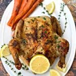 air fryer whole chicken on a white plate with fresh lemon and roasted carrots