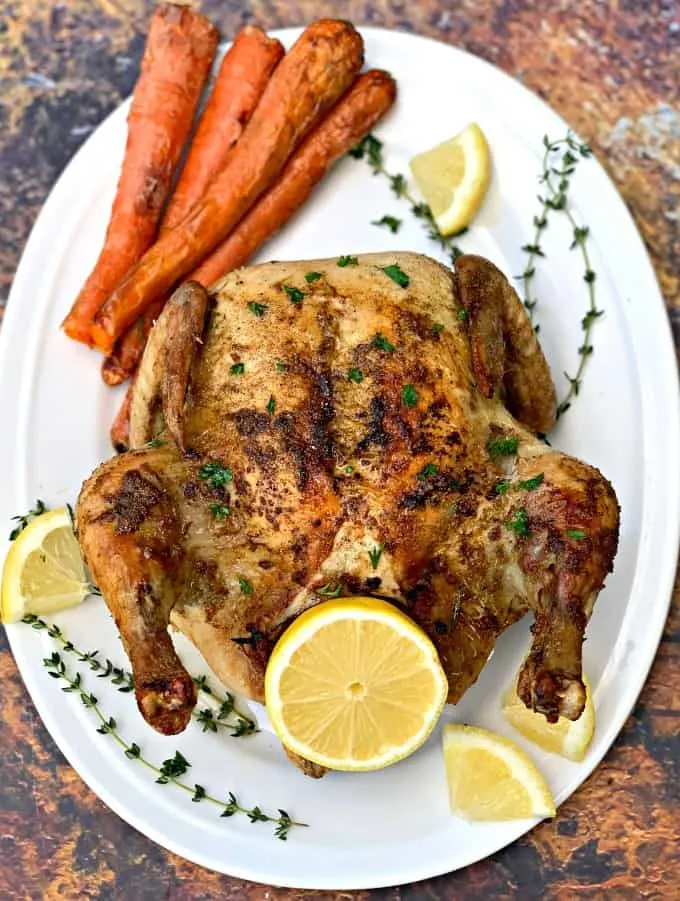 air fryer whole chicken on a white plate with fresh lemon and roasted carrots