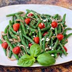 cold green bean salad with tomatoes and feta cheese on a white plate