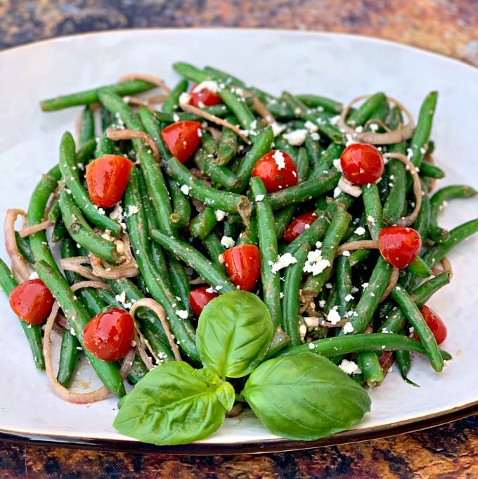 cold green bean salad with tomatoes and feta cheese on a white plate