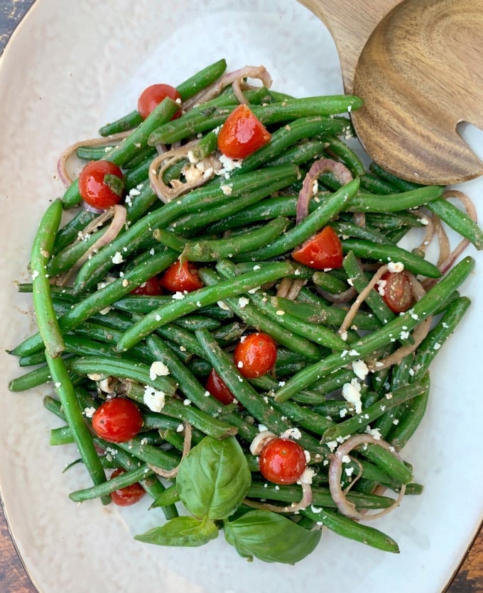 cold green bean salad with tomatoes and feta cheese on a white plate