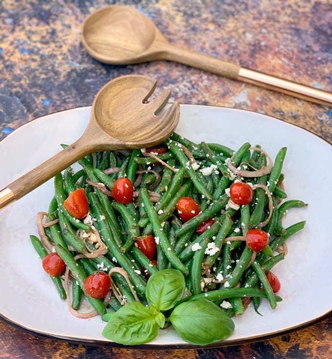 cold green bean salad with tomatoes and feta cheese on a white plate