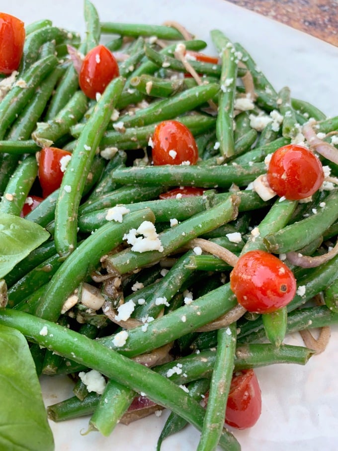 cold green bean salad with tomatoes and feta cheese on a white plate