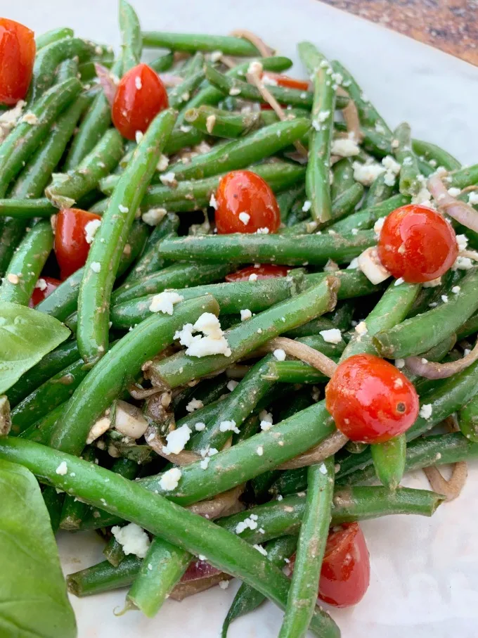 cold green bean salad with tomatoes and feta cheese on a white plate