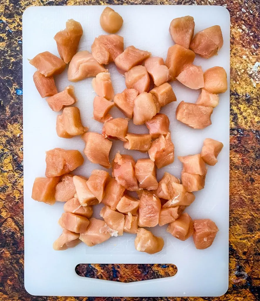 raw chicken sliced into cubes on a cutting board