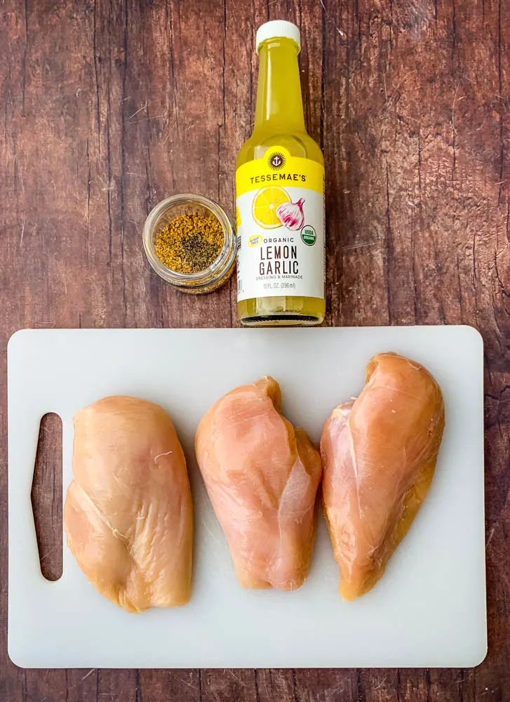 raw chicken breasts on a cutting board and lemon garlic marinade with seasoning in a glass bowl