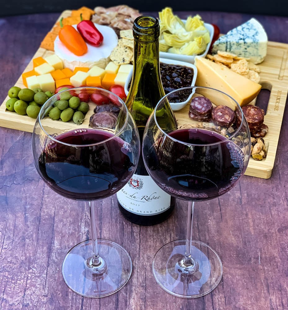 charcuterie board with artichokes, fig spread, cheese, and meat with 2 glasses of red wine