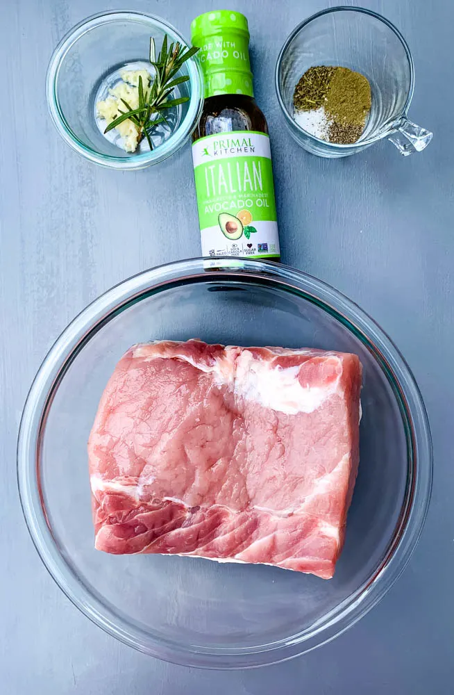 raw pork loin roast, Italian dressing, and seasoning in glass containers