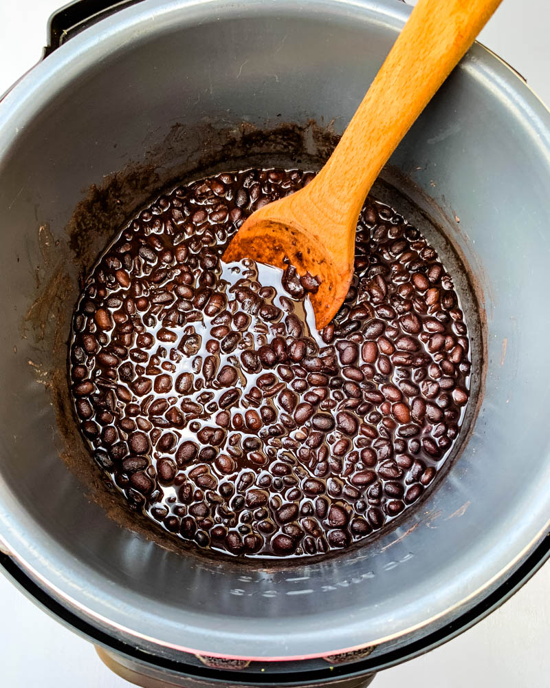cooked black beans in an instant pot with a wooden spoon