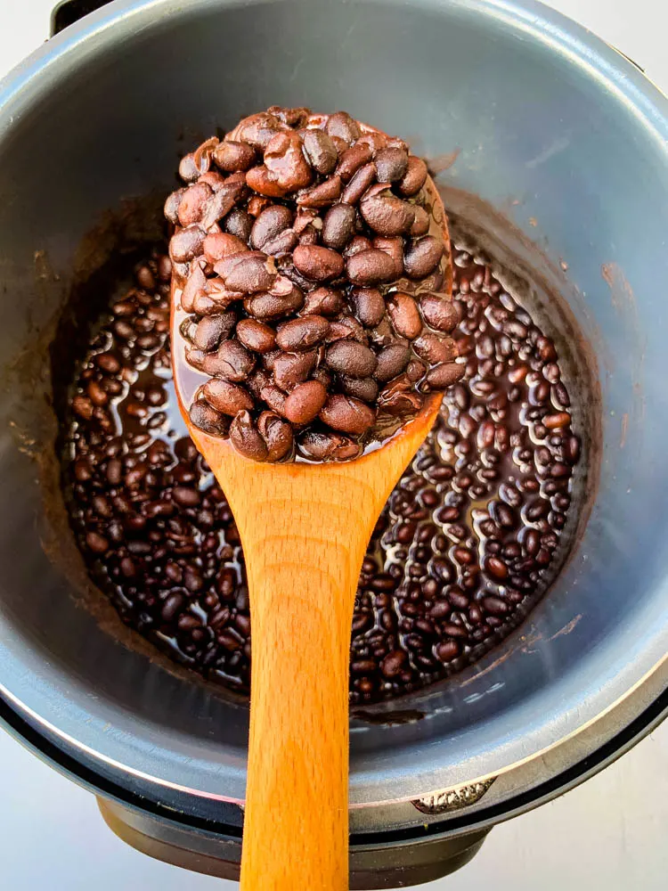 wooden spoon full of cooked black beans in an instant pot