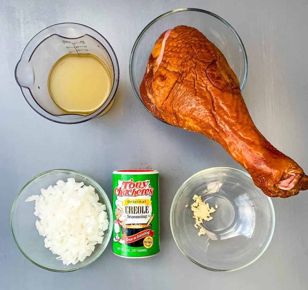 chicken broth, chopped onions and garlic, a smoked turkey leg, and Creole seasoning on a flat surface