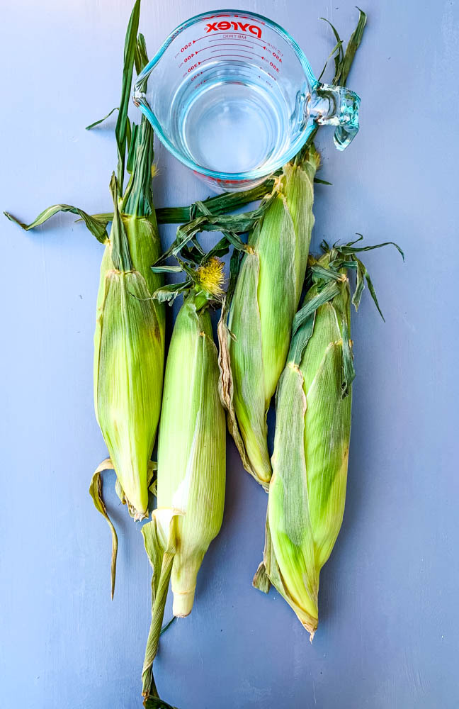 raw unshucked corn and 1 cup of water in a cup