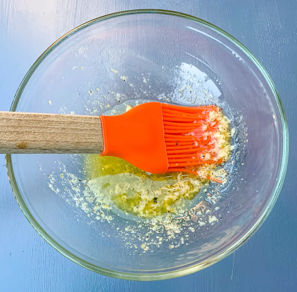 garlic butter sauce in a glass bowl with a cooking brush