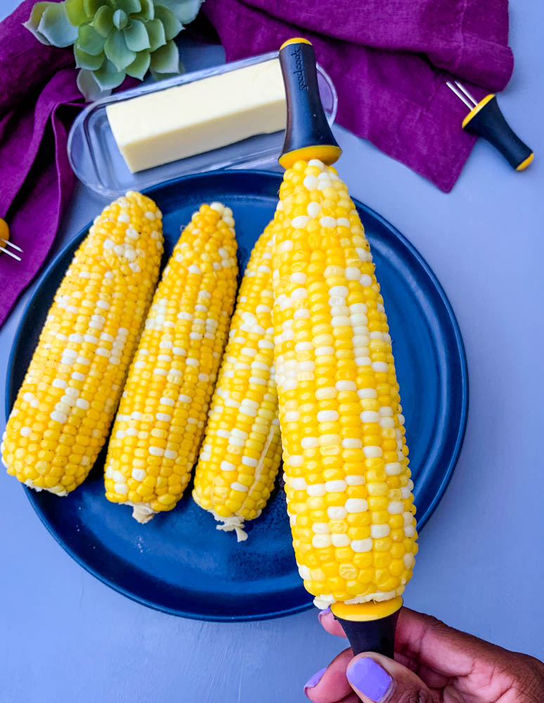 person holding instant pot corn on the cob on a blue plate with a purple napkin