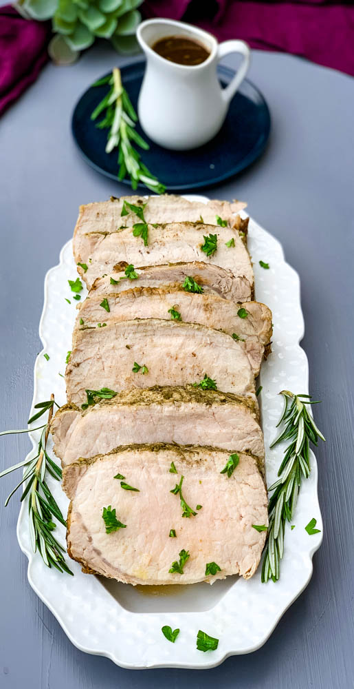 cooked sliced Instant Pot pork loin on a white plate with rosemary