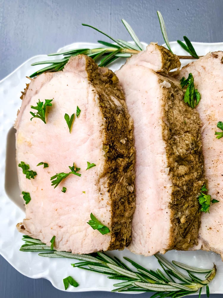 cooked sliced Instant Pot pork loin on a white plate with rosemary