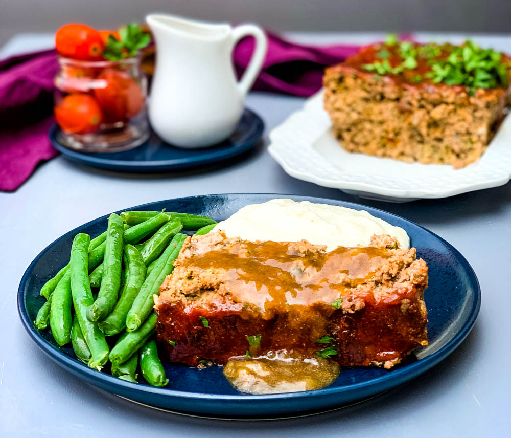 sliced keto low carb meatloaf on a blue plate with mashed cauliflower and blanched green beans