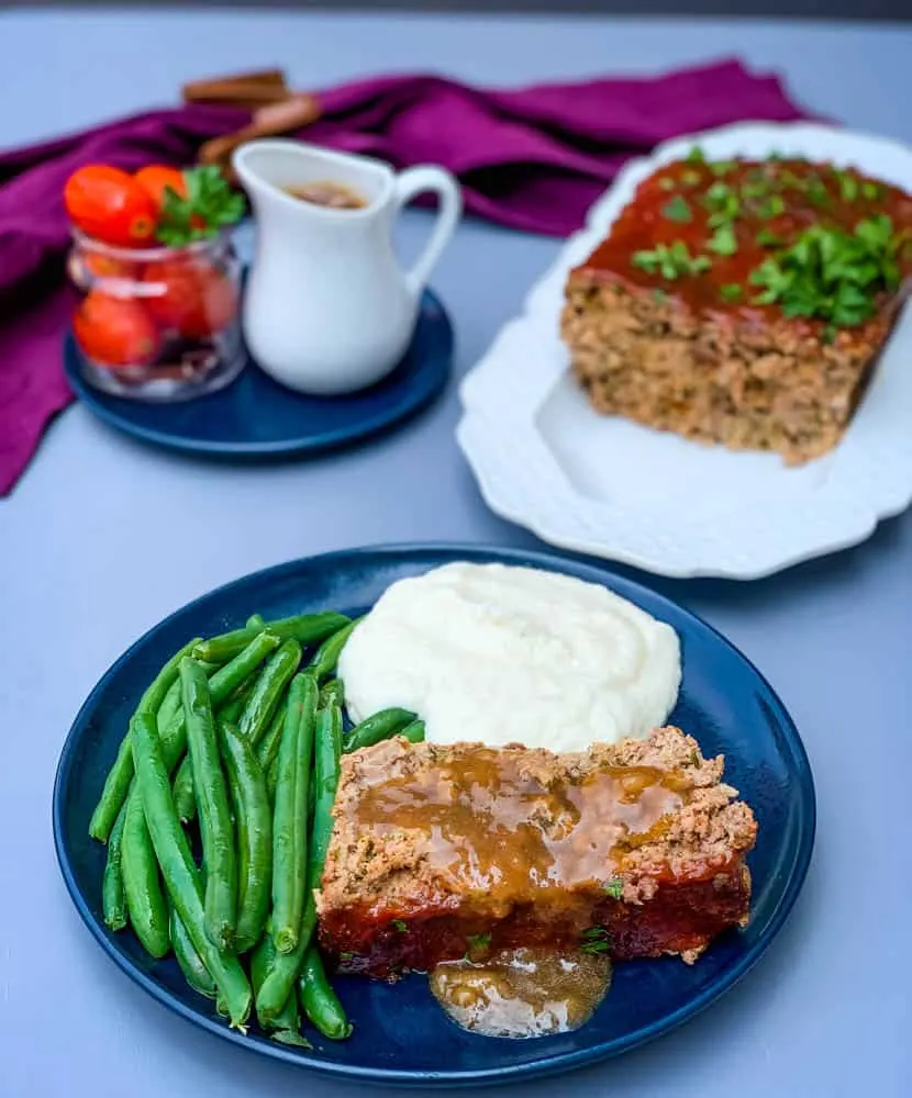 sliced keto low carb meatloaf on a blue plate with mashed cauliflower and blanched green beans