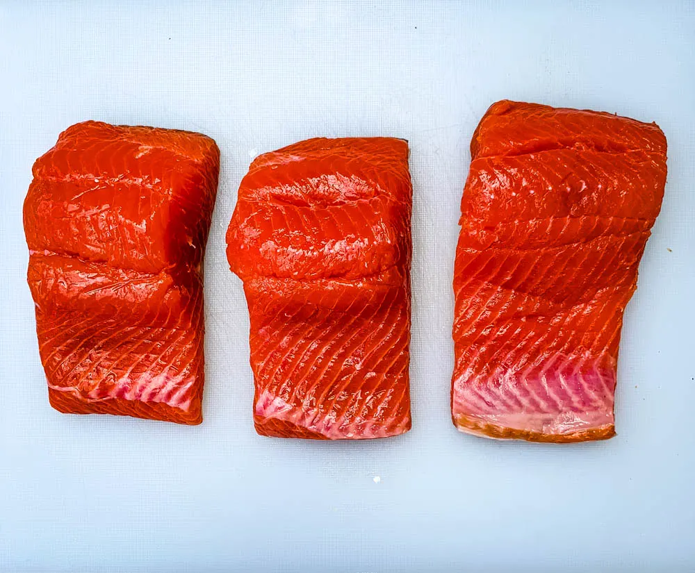 raw salmon fillets on a white cutting board
