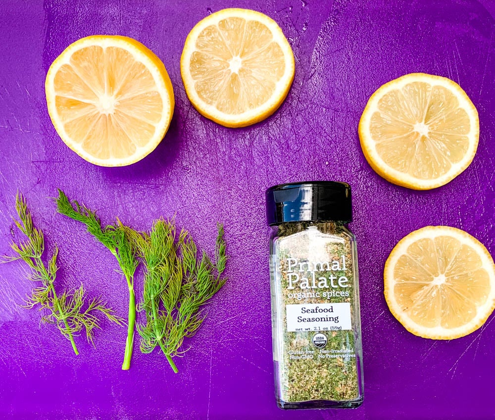 fresh lemon and dill on a purple cutting board with a bottle of seasoning