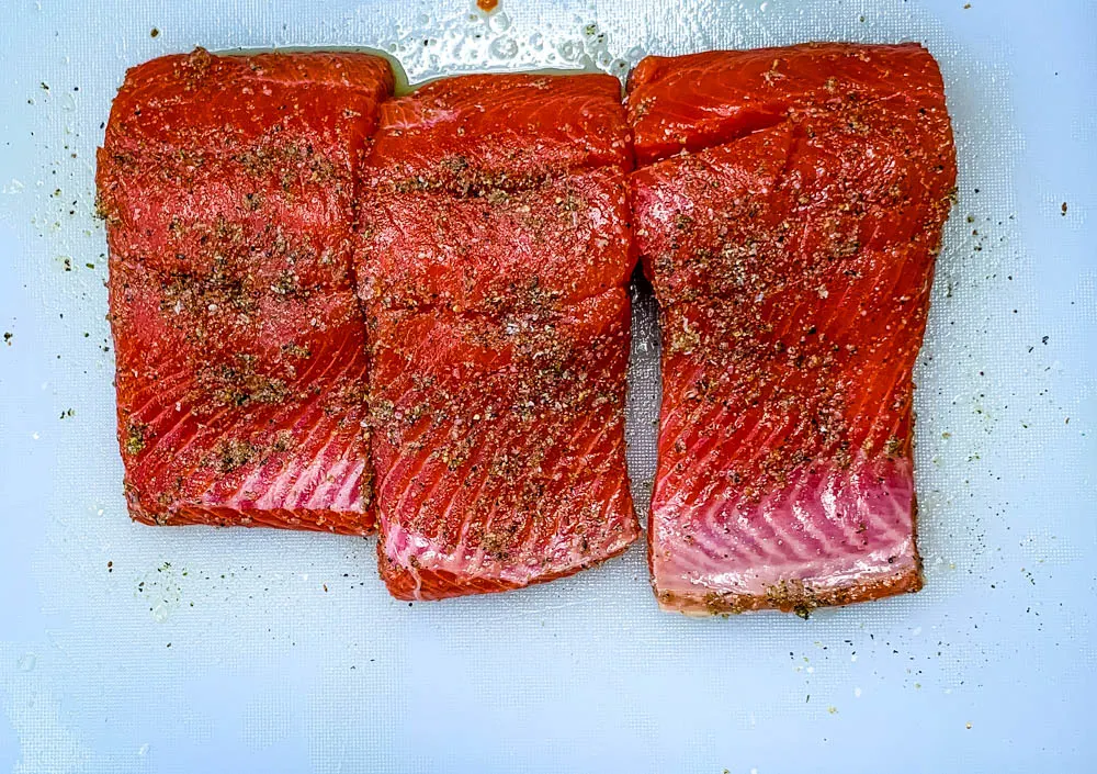 raw seasoned salmon fillets on a cutting board