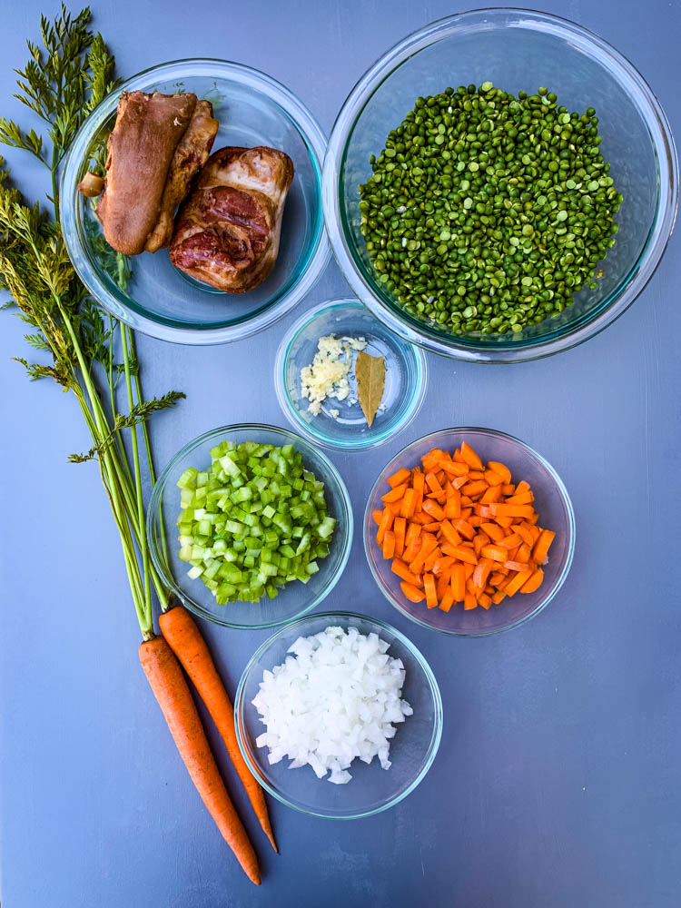 carrots, onions, celery, garlic, split peas, and ham hocks on a flat surface