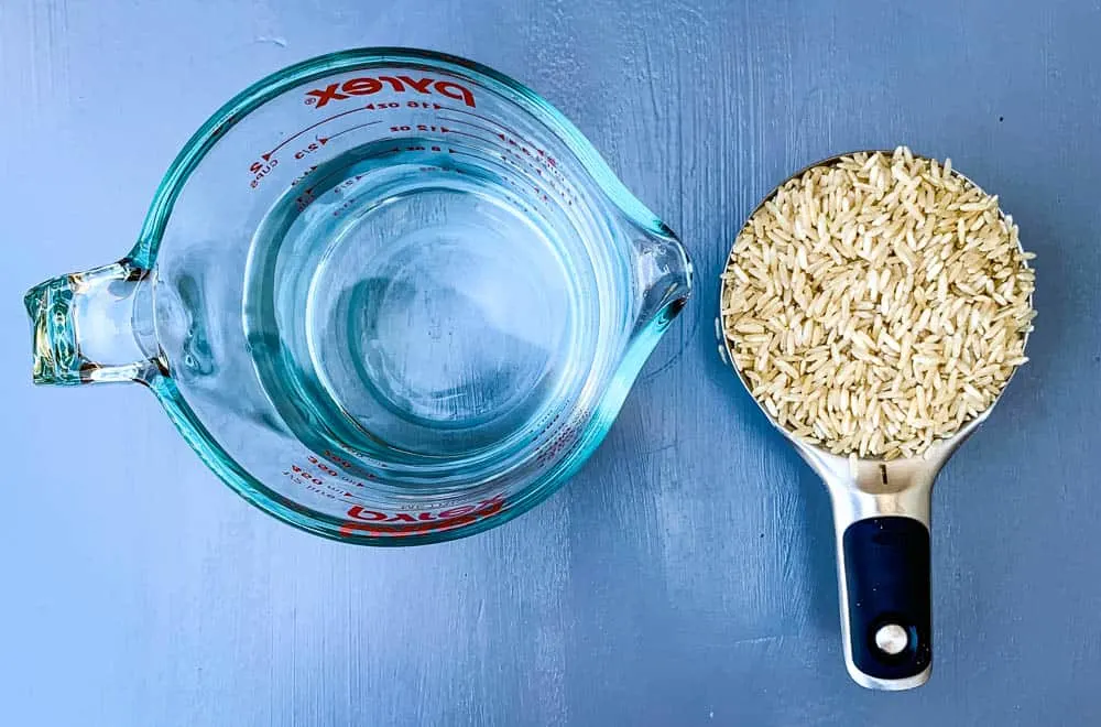 dry brown rice in a measuring cup and a cup of water