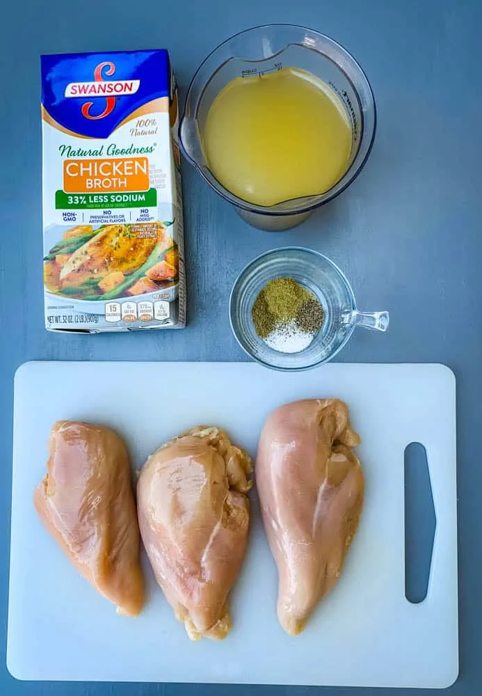 raw chicken breasts on a cutting board with chicken broth and spices and herbs