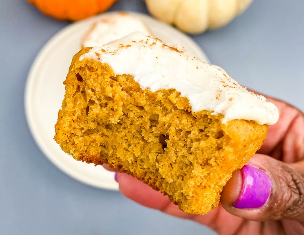 person holding half eaten keto pumpkin muffin with cream cheese