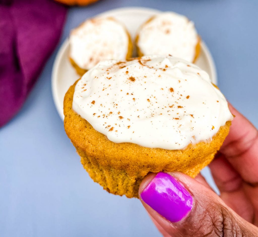 person holding keto pumpkin muffin with cream cheese frosting
