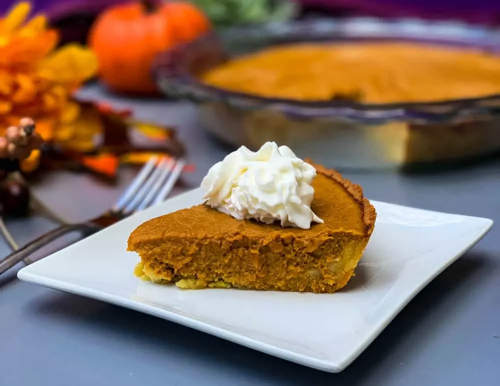 keto low carb pumpkin pie on a white plate with a whole cut pie in the back