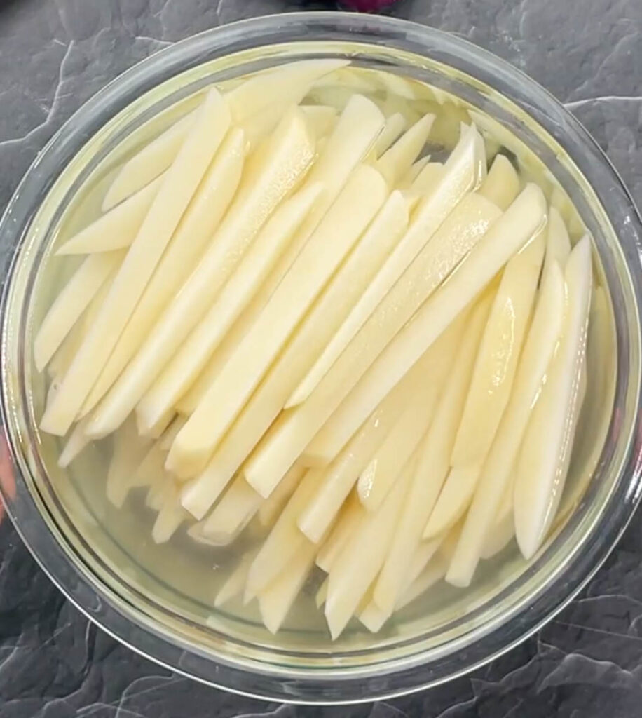 sliced potatoes in a glass bowl of water