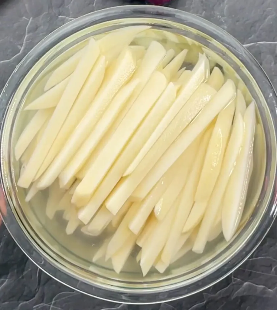 sliced potatoes in a glass bowl of water