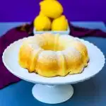 air fryer lemon cake on a white cake stand with fresh lemons